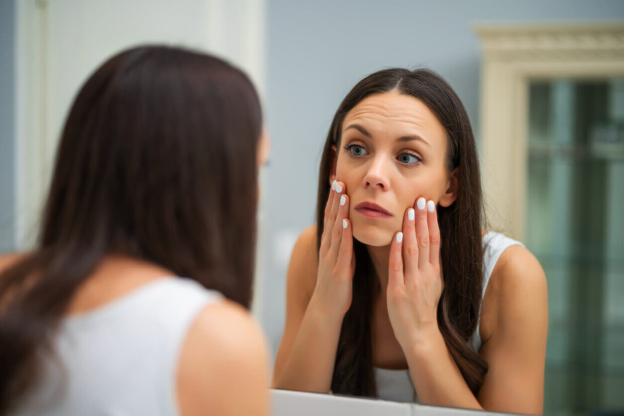 mulher no espelho vendo sinais de fadiga facial.