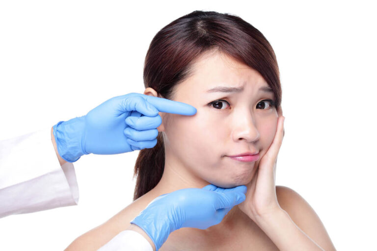 Mulher com expressão de dor enquanto profissional de saúde aponta para sua bochecha, simbolizando avaliação prévia ao procedimento de bichectomia.