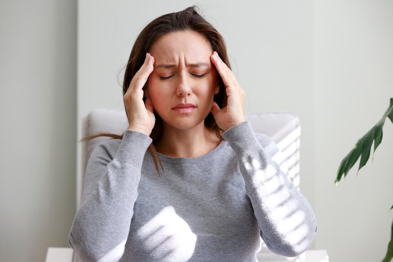 Mulher com expressão de dor, pressionando as têmporas com as mãos, sugerindo dor de cabeça intensa ou enxaqueca. Precisando de botox para dor de cabeça.