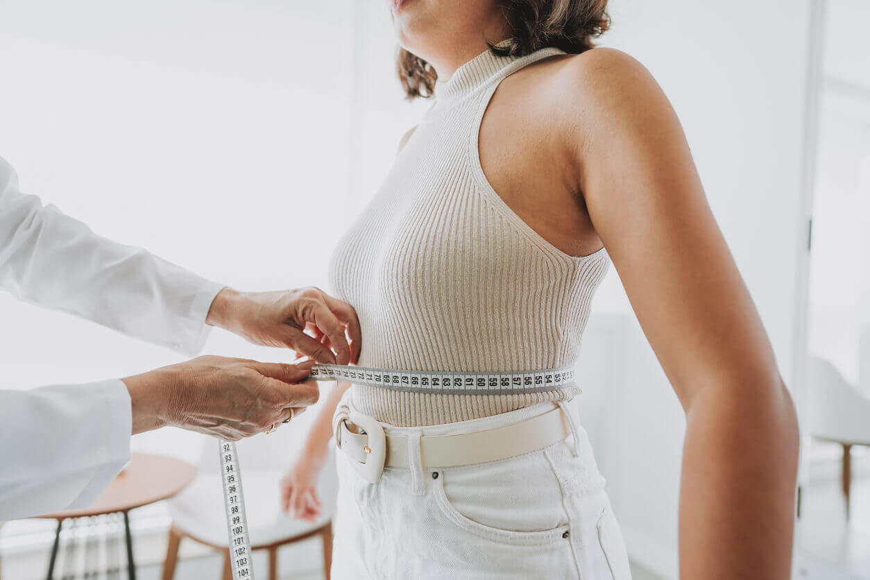 Mulher sendo medida com fita métrica na cintura durante consulta médica, simbolizando o acompanhamento de peso após cirurgia bariátrica. Mulher querendo estabilzar o peso.