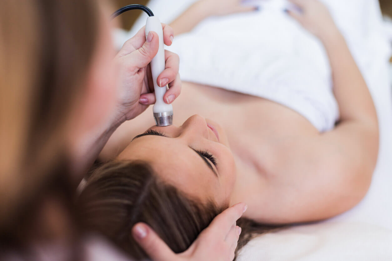 Mulher deitada em maca estética recebe tratamento facial com aparelho de radiofrequência, voltado para suavização de cicatriz de queimadura no rosto.
