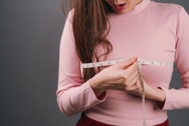 Mulher medindo o busto com fita métrica, ilustrando o interesse pelos benefícios da mamoplastia redutora para estética e saúde