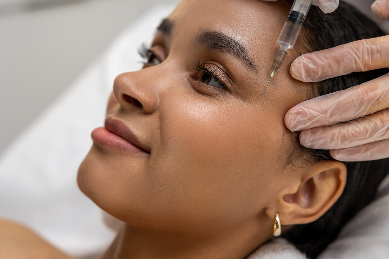 Mulher sorrindo durante aplicação de injeção estética na testa, representando procedimentos estéticos em alta entre famosas