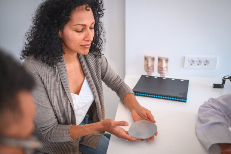 Mulher em consulta médica segurando prótese de silicone nas mãos antes de decidir sobre colocar silicone