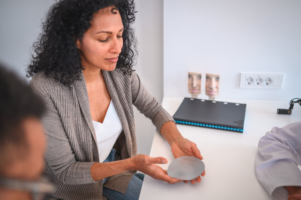 Mulher em consulta médica segurando prótese de silicone nas mãos antes de decidir sobre colocar silicone