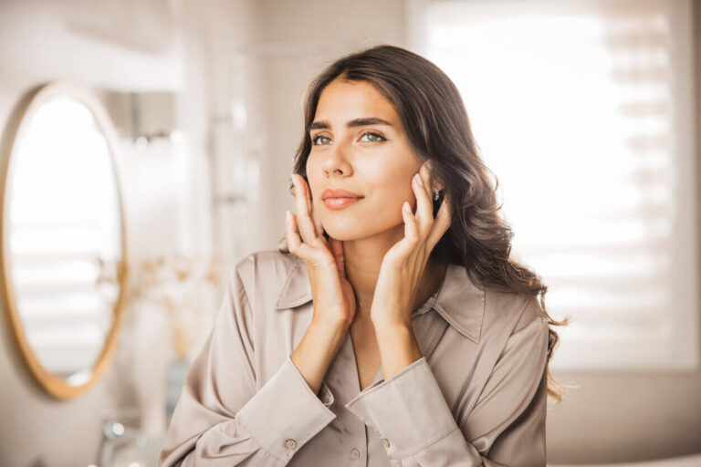 Mulher olhando-se no espelho após realizar bichectomia e lifting facial, exibindo contornos faciais mais definidos e pele com aparência rejuvenescida.