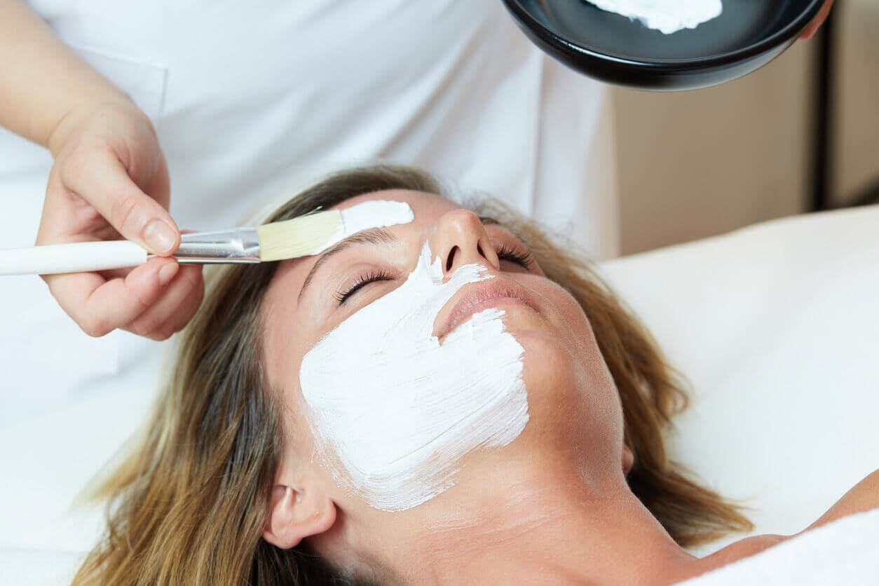 mulher recebendo peeling químico facial com aplicação de máscara esbranquiçada por profissional de estética