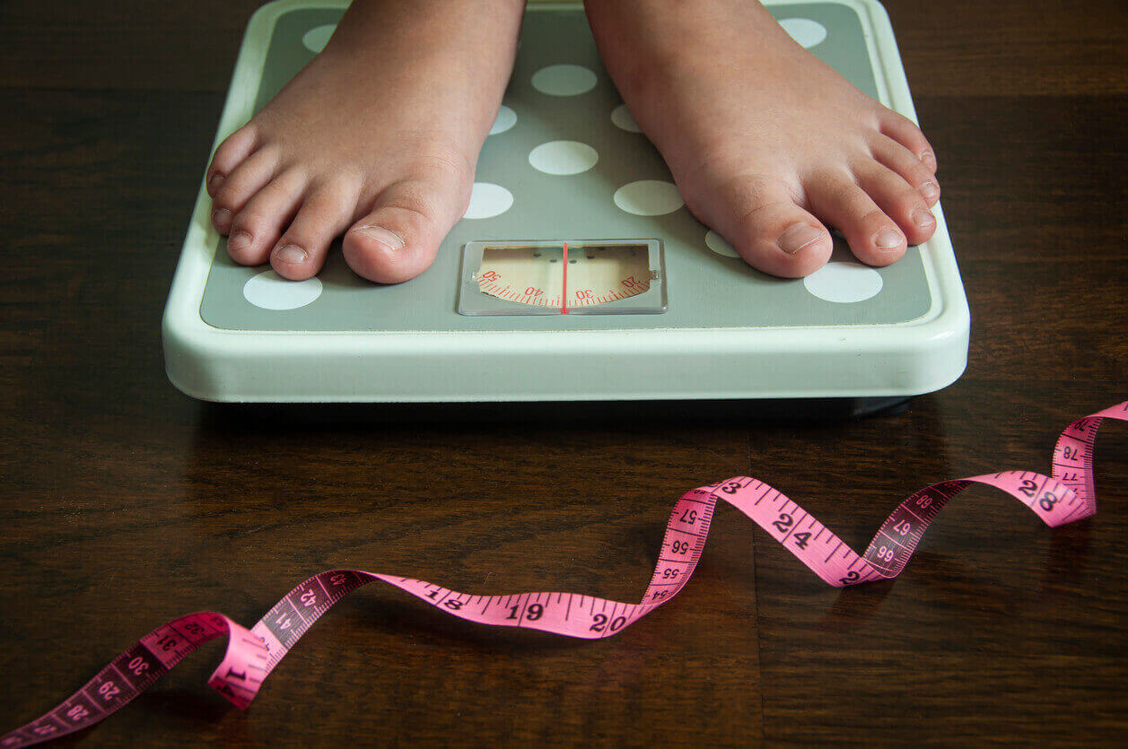 Criança em pé sobre balança com fita métrica no chão, imagem usada para ilustrar lipedema em crianças e alterações corporais precoces