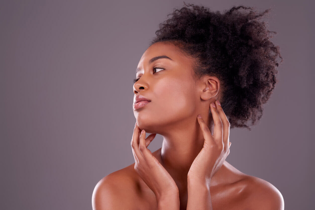Mulher tocando o rosto e o contorno da mandíbula, ilustrando alterações faciais associadas ao rosto de ozempic após emagrecimento rápido