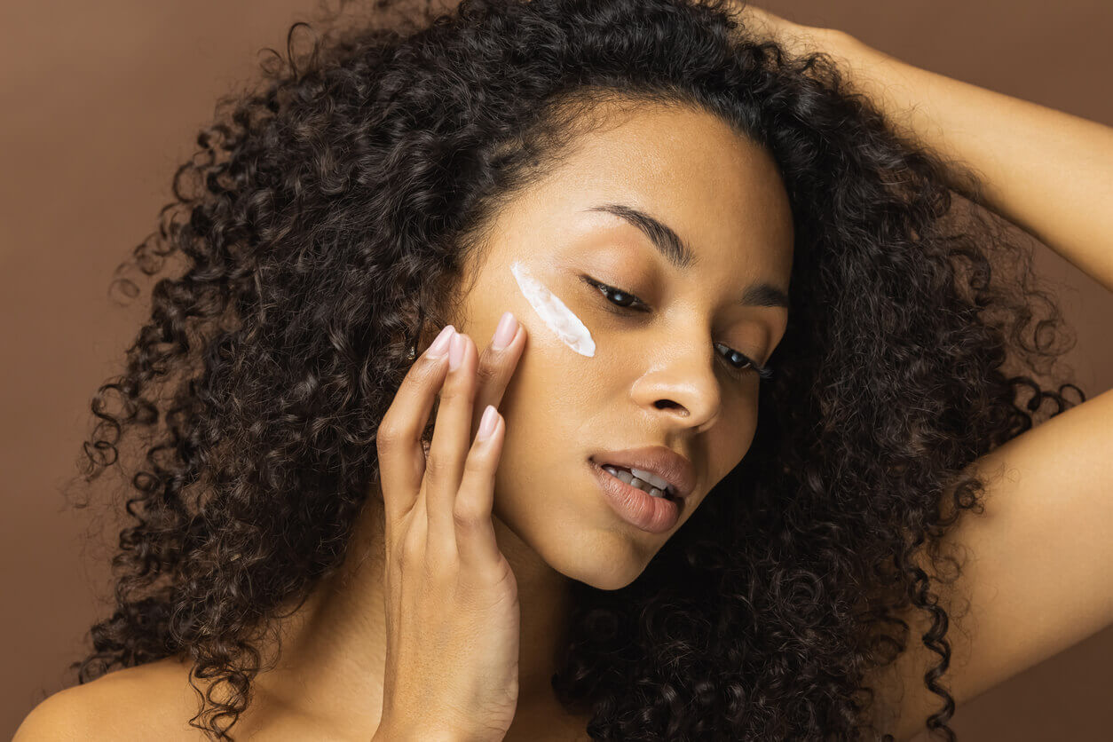 Mulher aplicando creme facial durante cuidados de tratamento para manchas no rosto.