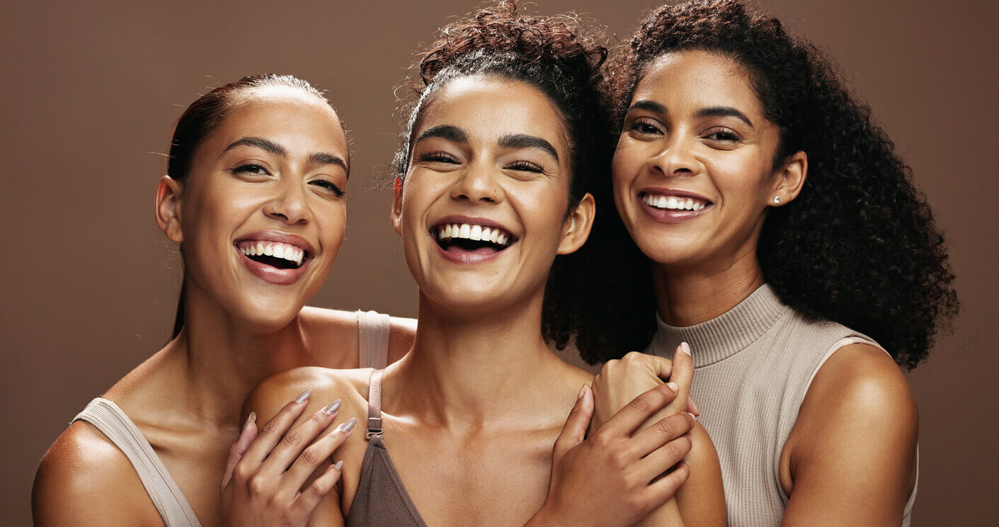 Três mulheres sorrindo lado a lado, representando diferentes características faciais em conteúdo sobre cirurgia lifting facial e abordagens individualizadas.