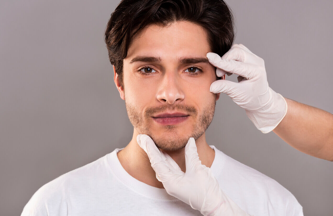 Homem durante avaliação estética facial para lifting facial masculino, com profissional analisando a região do rosto e mandíbula.