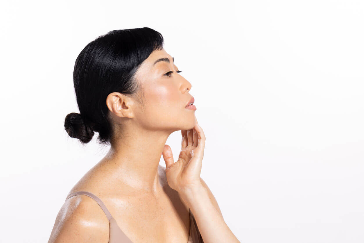 Mulher de perfil tocando a região da mandíbula, ilustrando conteúdo sobre preenchimento facial para definição do contorno facial.