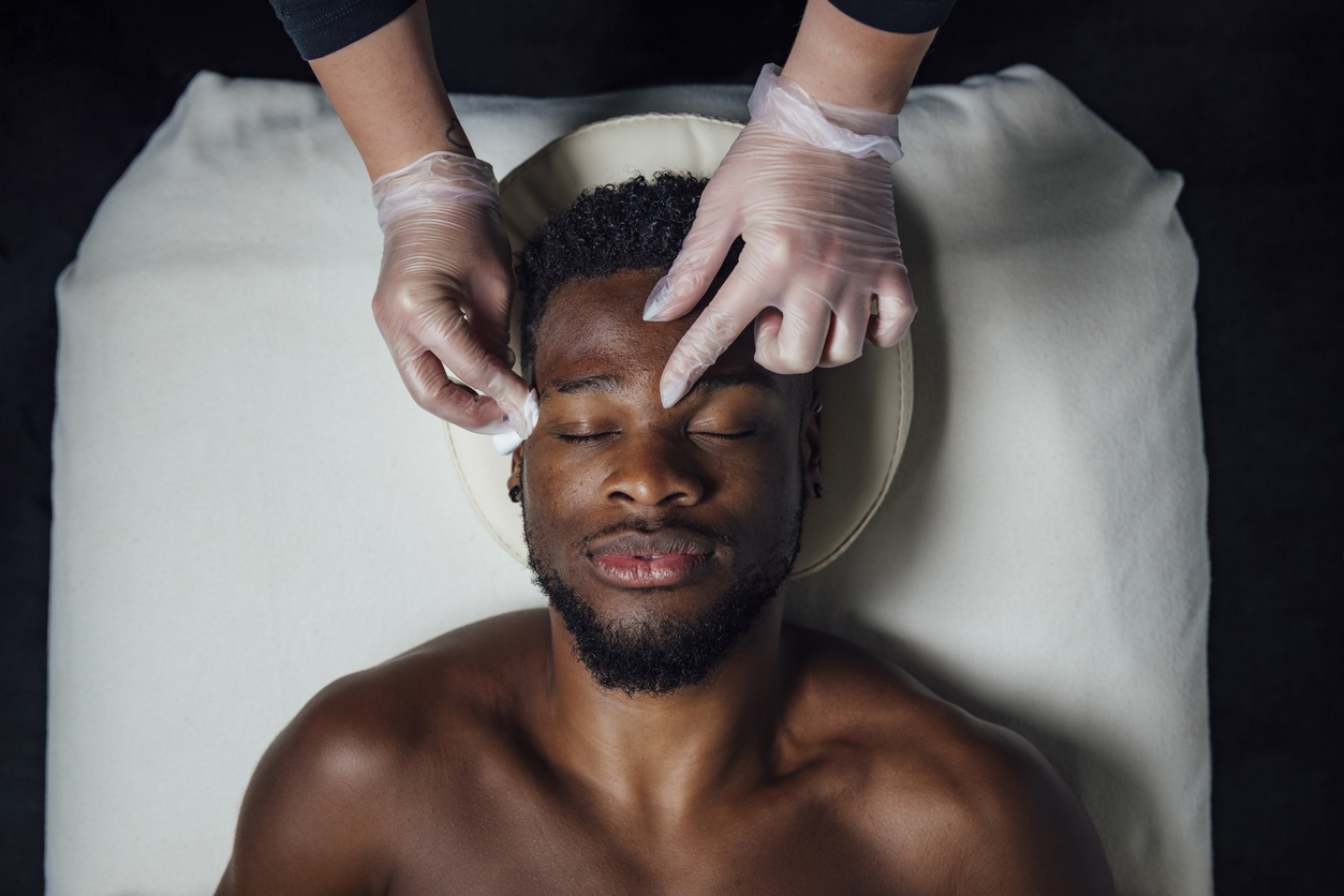 Homem recebe cuidados estéticos faciais durante procedimento em clínica, representando o crescimento da estética masculina.